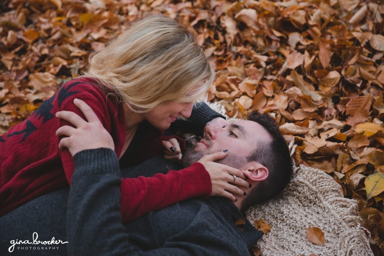 A romantic and natural photograph of a couple laying on a blanket on the fallen leaves during their fall couple session in Boston's Arnold Arboretum
