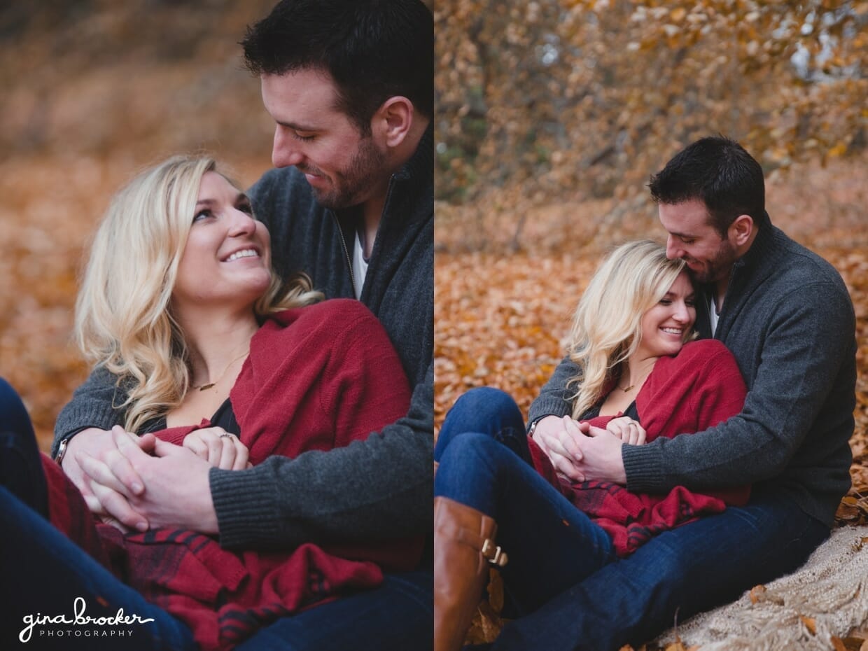 A cute photograph of couple cuddling and laughing as they sit on a blanket in the fallen leaves during their fall couple session in Boston's Arnold Arboretum