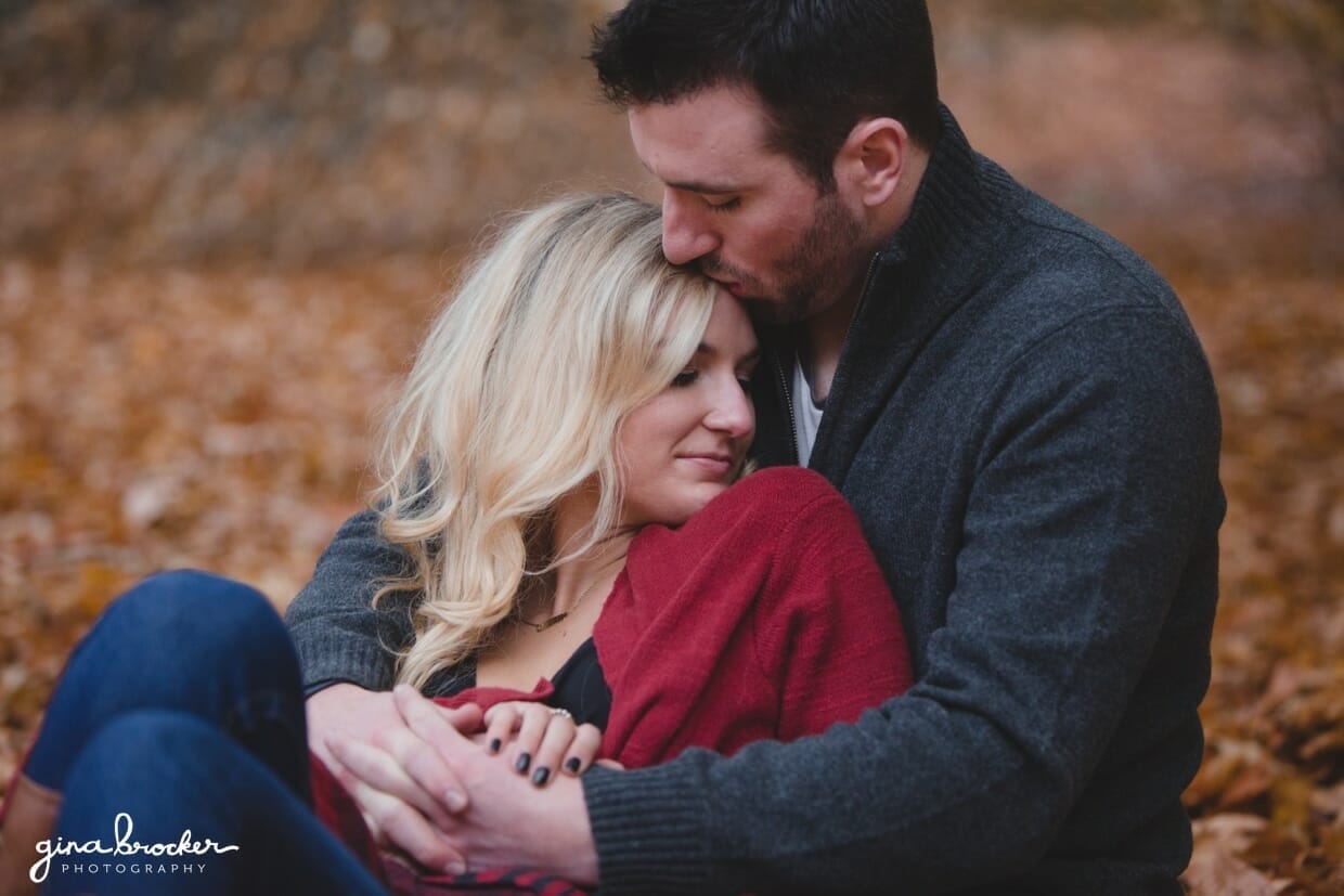 A romantic photograph of a couple cuddling amongst the fallen leaves during their fall engagement session in Boston's Arnold Arboretum
