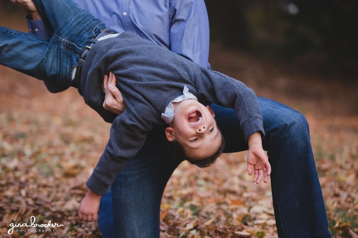 A fun photograph of a father playing with his son during their fall family photo session in the Arnold Arboretum in Boston, Massachusetts