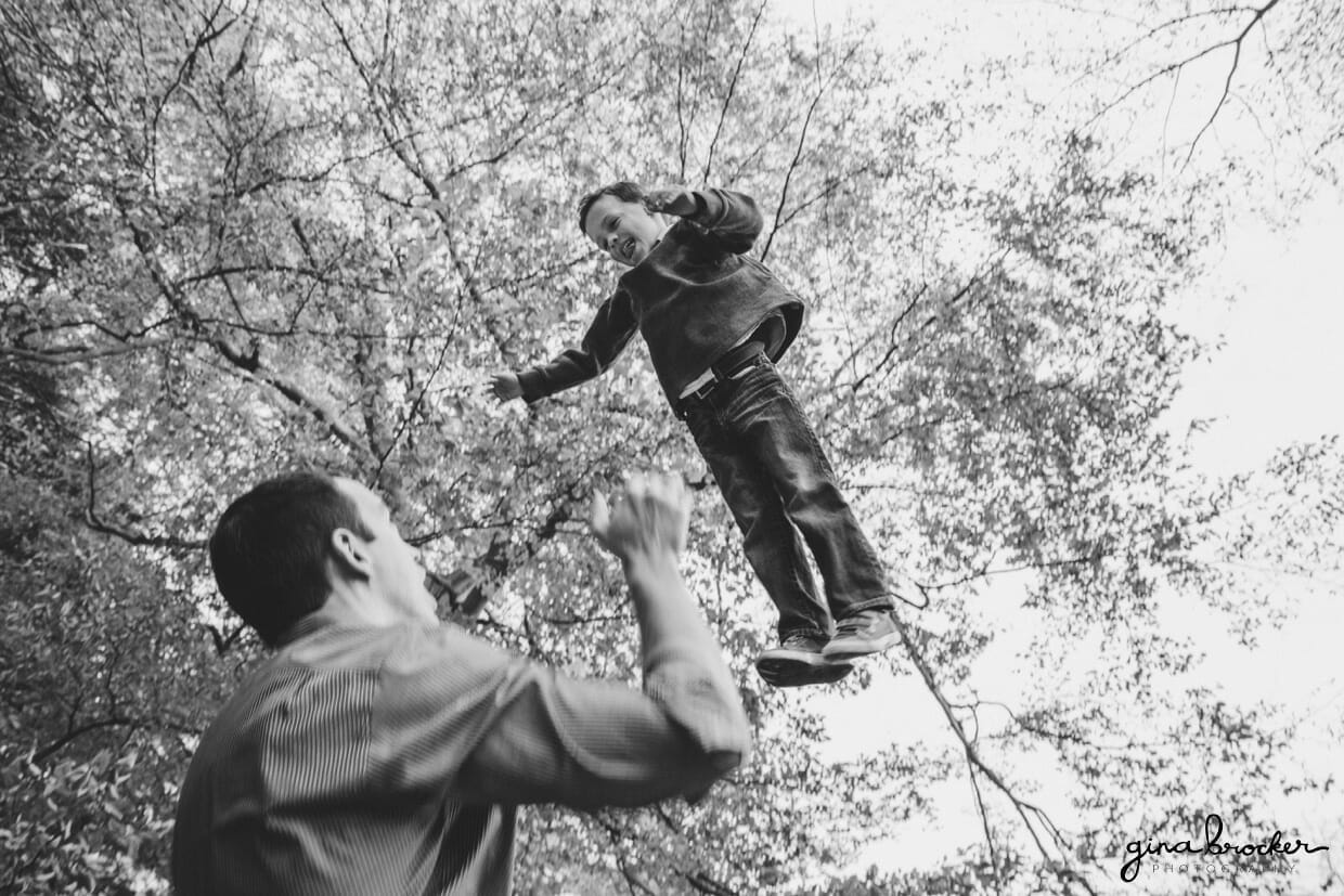A fun photograph of a father throwing his son into the air during their family photo session in the Arnold Arboretum in Boston, Massachusetts