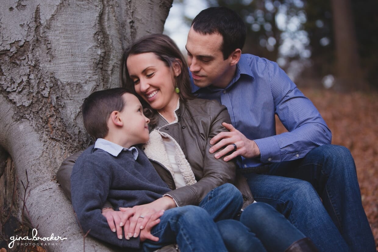 A family cuddles together against a tree in the park during their fall family photo session in Boston