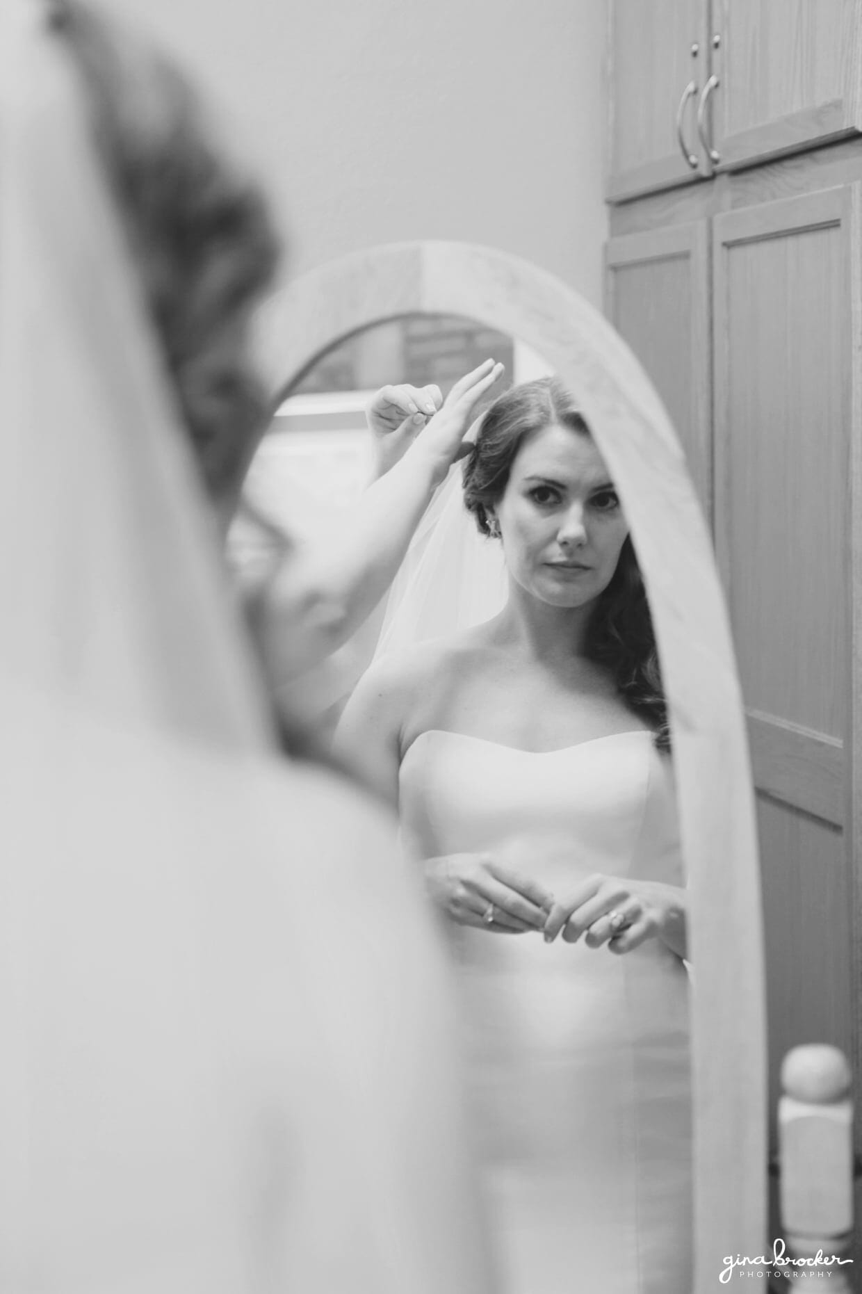 Bride looks in the mirror as she puts on her veil before the ceremony of her classic and elegant wedding in Boston, Massachusetts