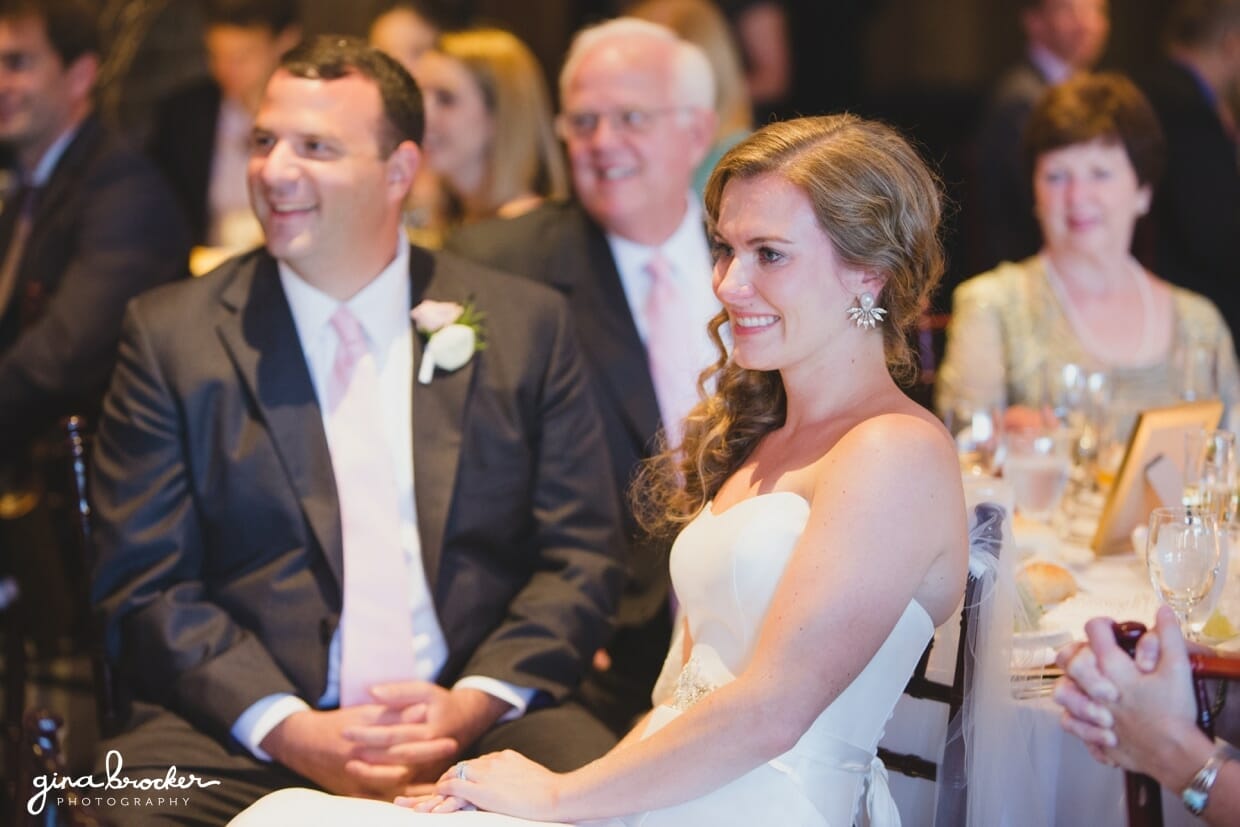 The bride and groom smile during the speeches at their elegant and classic Boston wedding in Massachusetts