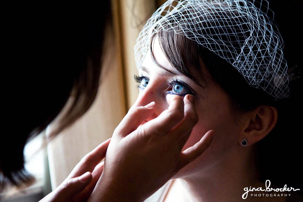 A candid photograph of a bride getting her bridal makeup done on the morning of her wedding