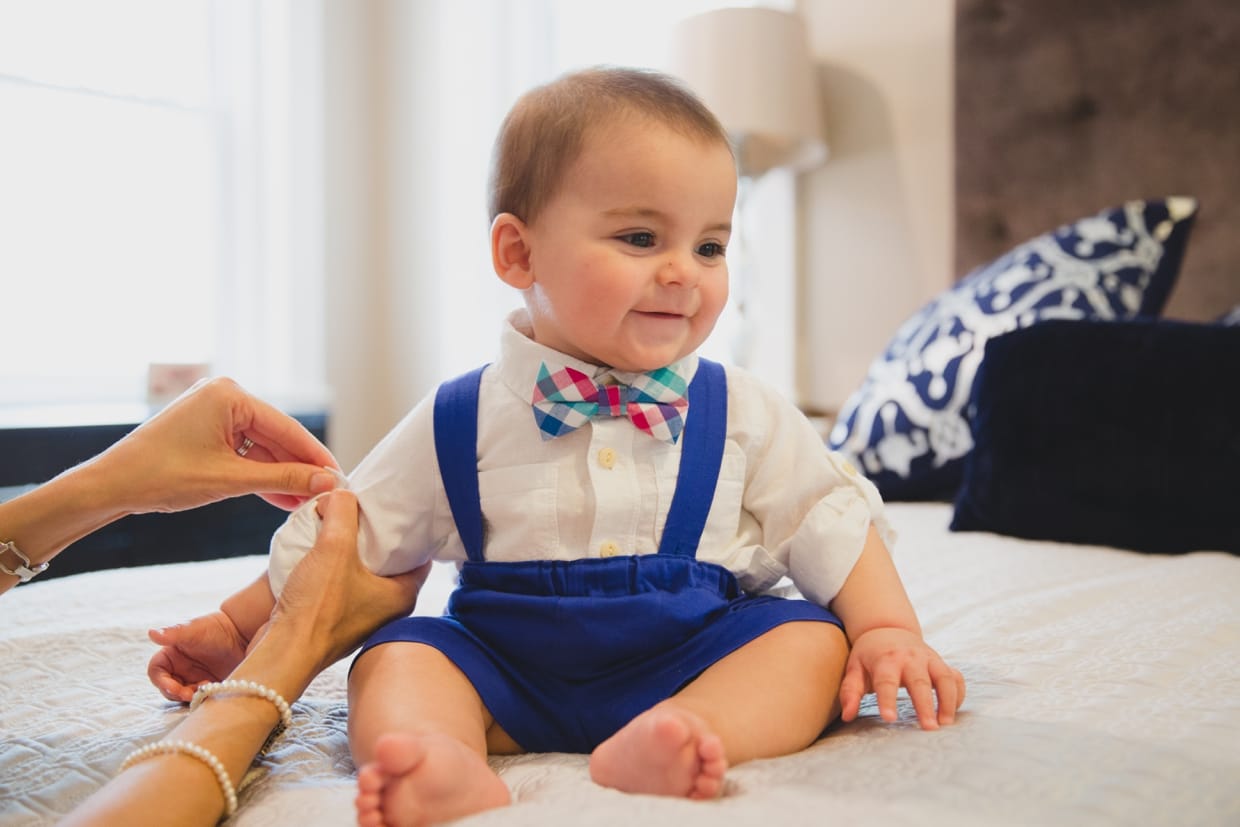 A baby boy smiles while getting dressed during a Boston family photo session at home.