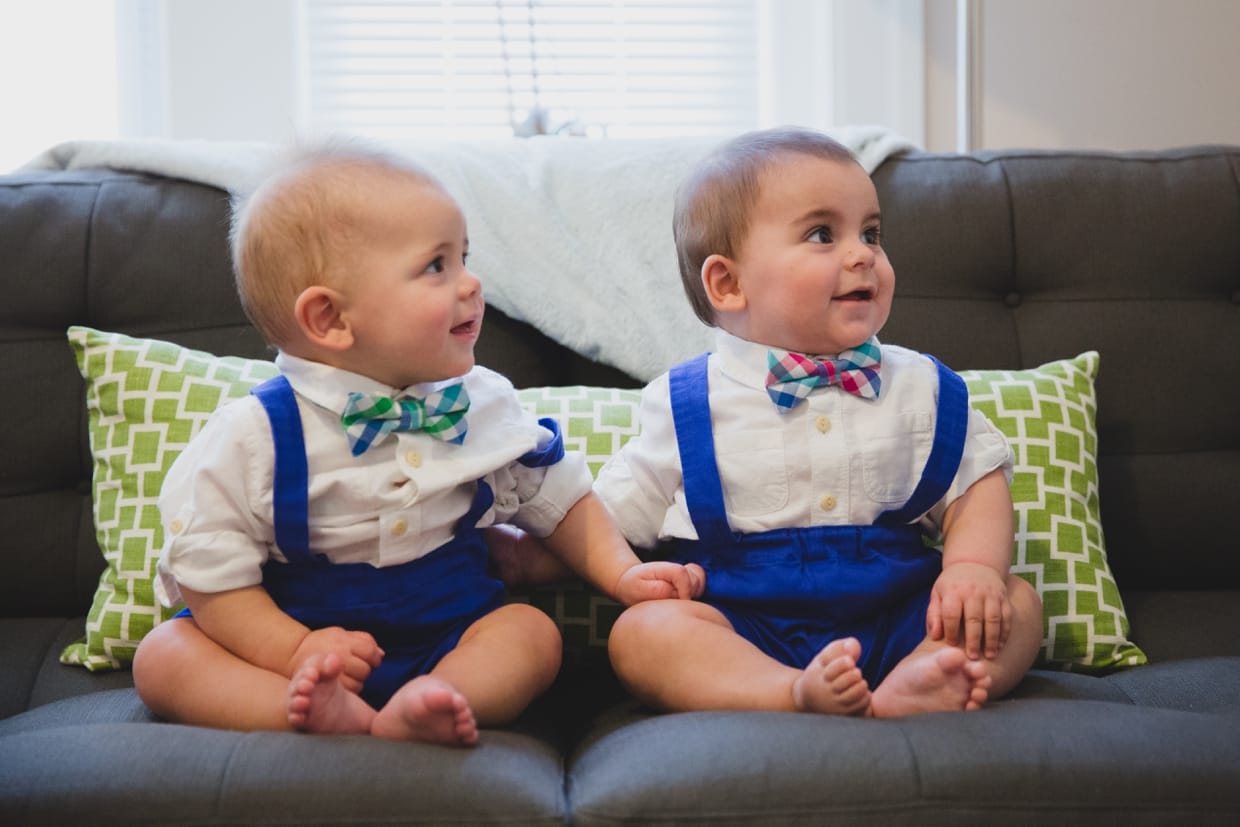 A candid portrait of twin baby boys sitting on the couch during a family photo session at home.
