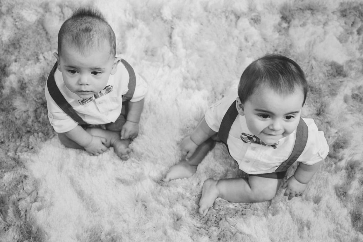 A candid portrait of twin baby boys sitting on the floor during their Boston in home family photo session.