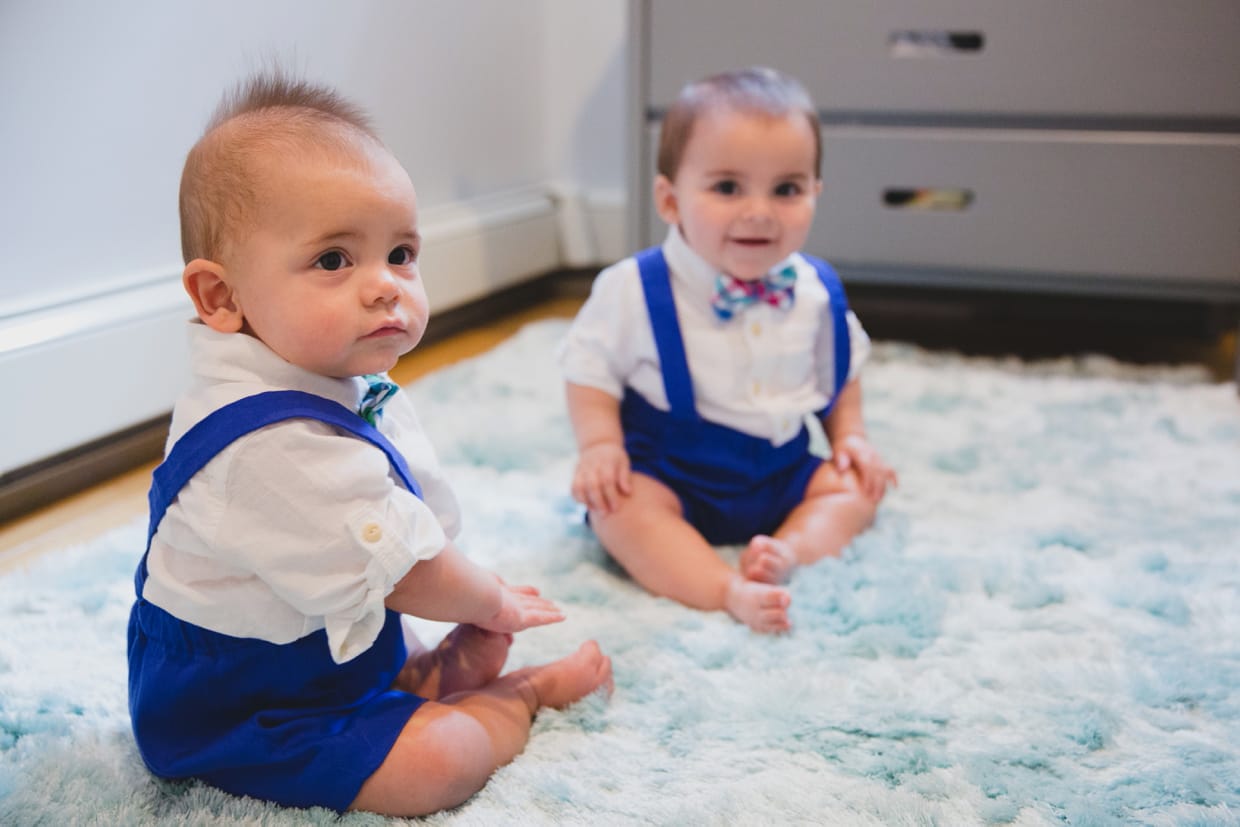 A candid portrait of twin baby boys sitting on the floor during a in home family photo session in Boston.
