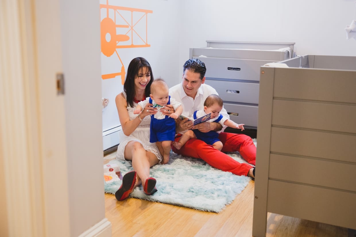 A documentary and candid photograph of parents reading a story to their twin baby boys during their in home family photo session in Boston