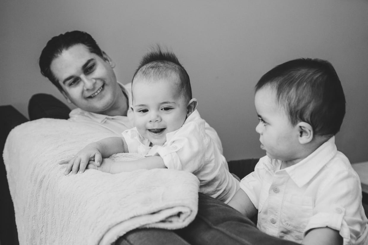 A documentary photograph of a father playing with his sons on their couch at home during a Boston family photo session.