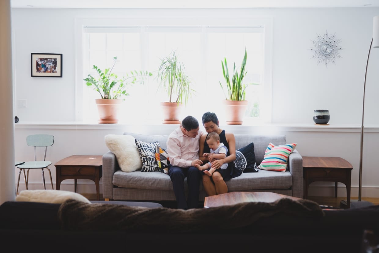 A candid photograph of a family sitting together on the couch during their documentary style in home family photo session in Boston's Jamaica Plain