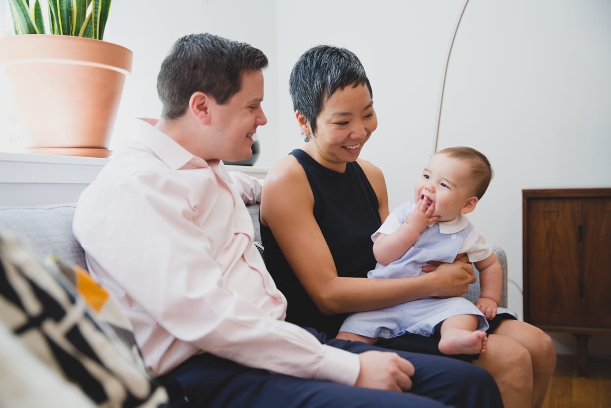 Parents play with their baby boy on the couch during an in home documentary family photo session in Jamaica Plain