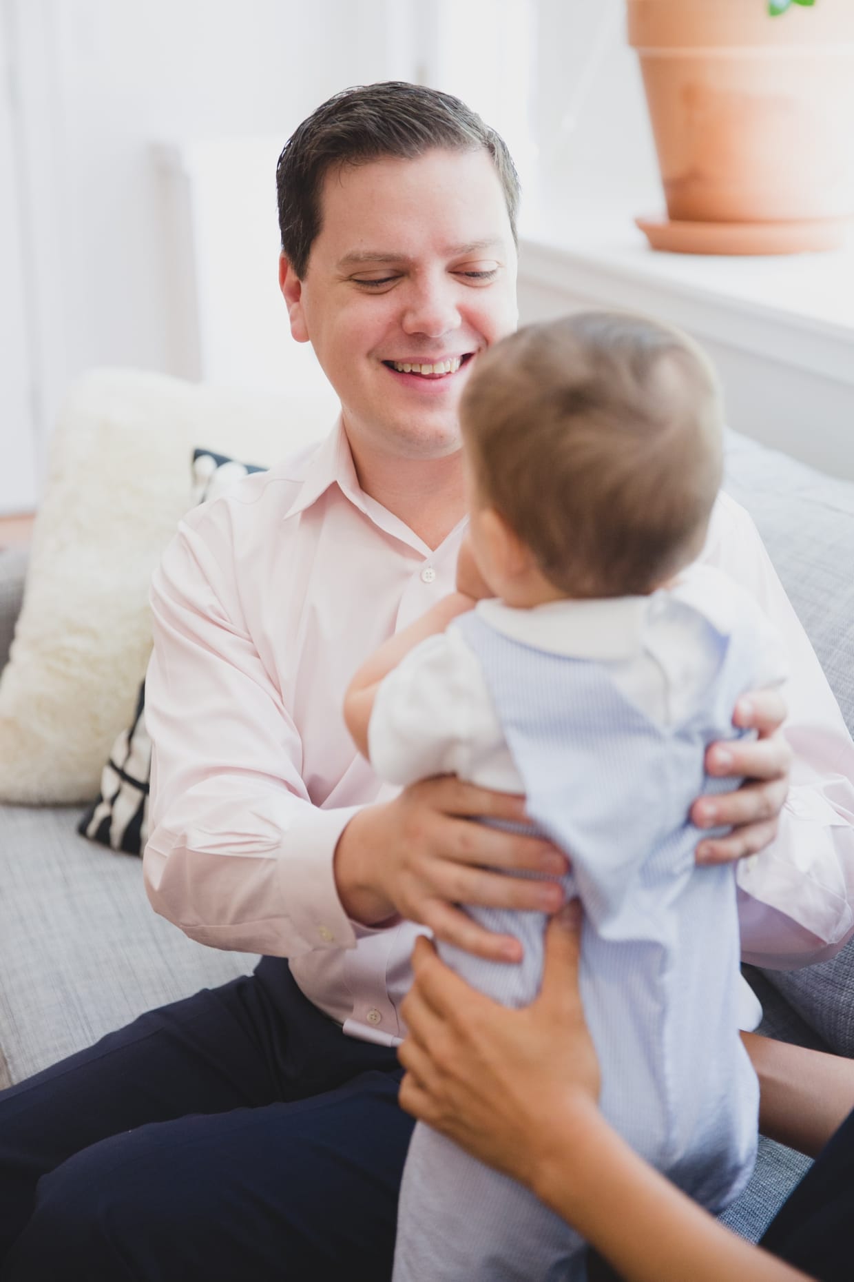 A father holds his baby boy while sitting on the couch during an in home family photo session in Jamaica Plain