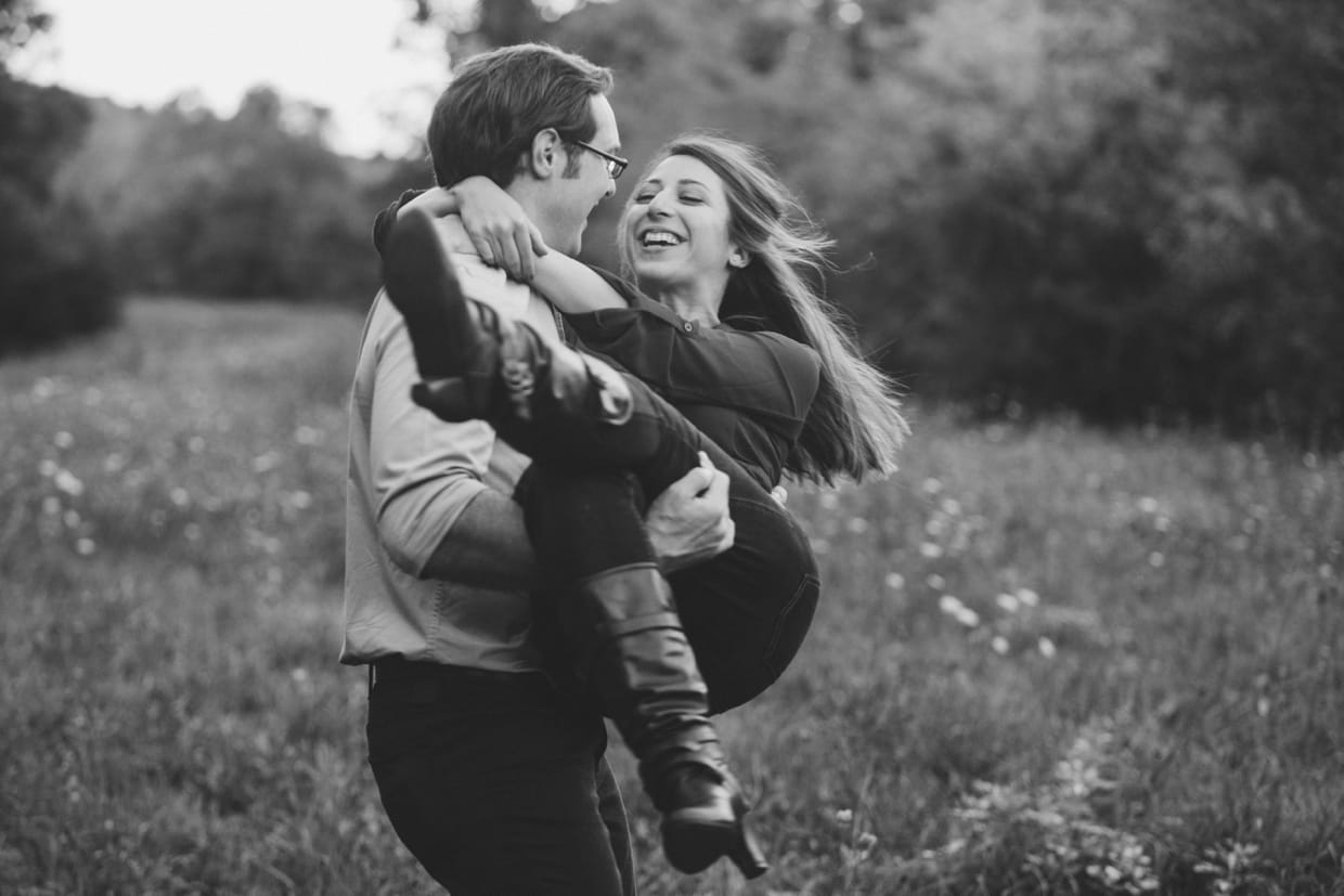 A fun photograph of a couple spinning around in a field during their Arnold Arboretum Engagement in Boston, Massachusetts