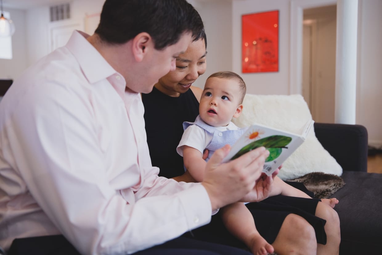 A sweet photograph of parents reading a book to their baby boy on the couch of their Jamaica Plain home during a in home family photo session