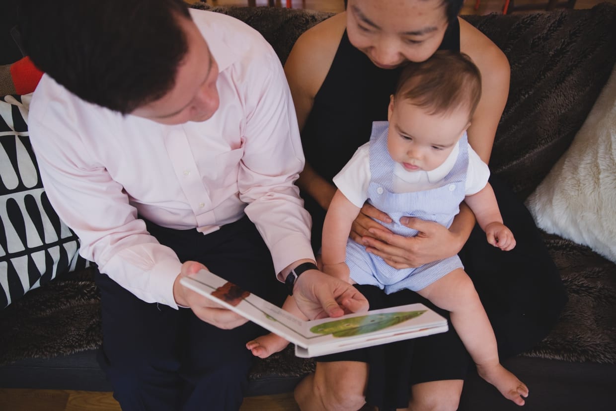 Artistic photograph of parents reading a book to their baby boy on the couch during their documentary in home family photo session