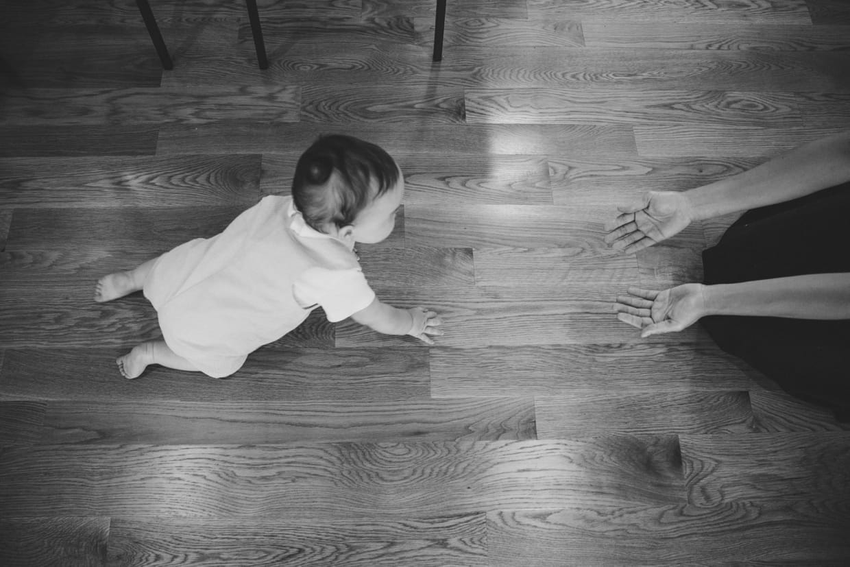 An artistic and candid photograph of a baby crawling towards his mother during their in home family photo session in Jamaica Plain