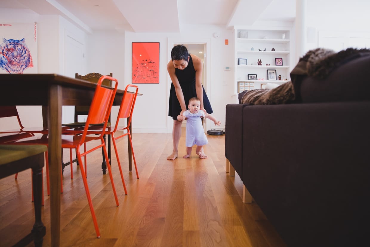 An amazing photograph of a mother helping her baby boy walk during their in home family photo session in Jamaica Plain
