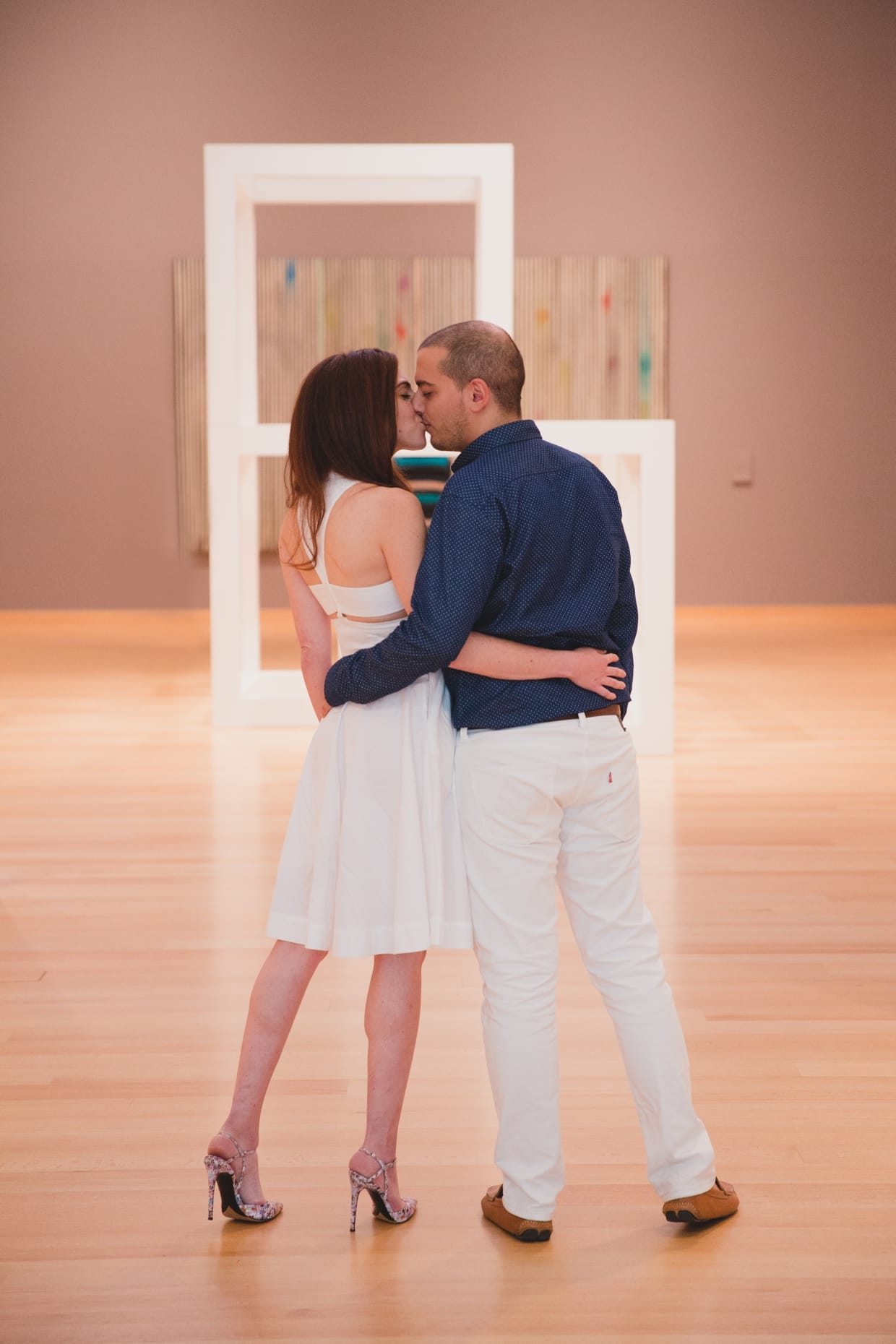 A couple kiss in front of the contemporary art display during their engagement session at the Boston Museum of Fine Art