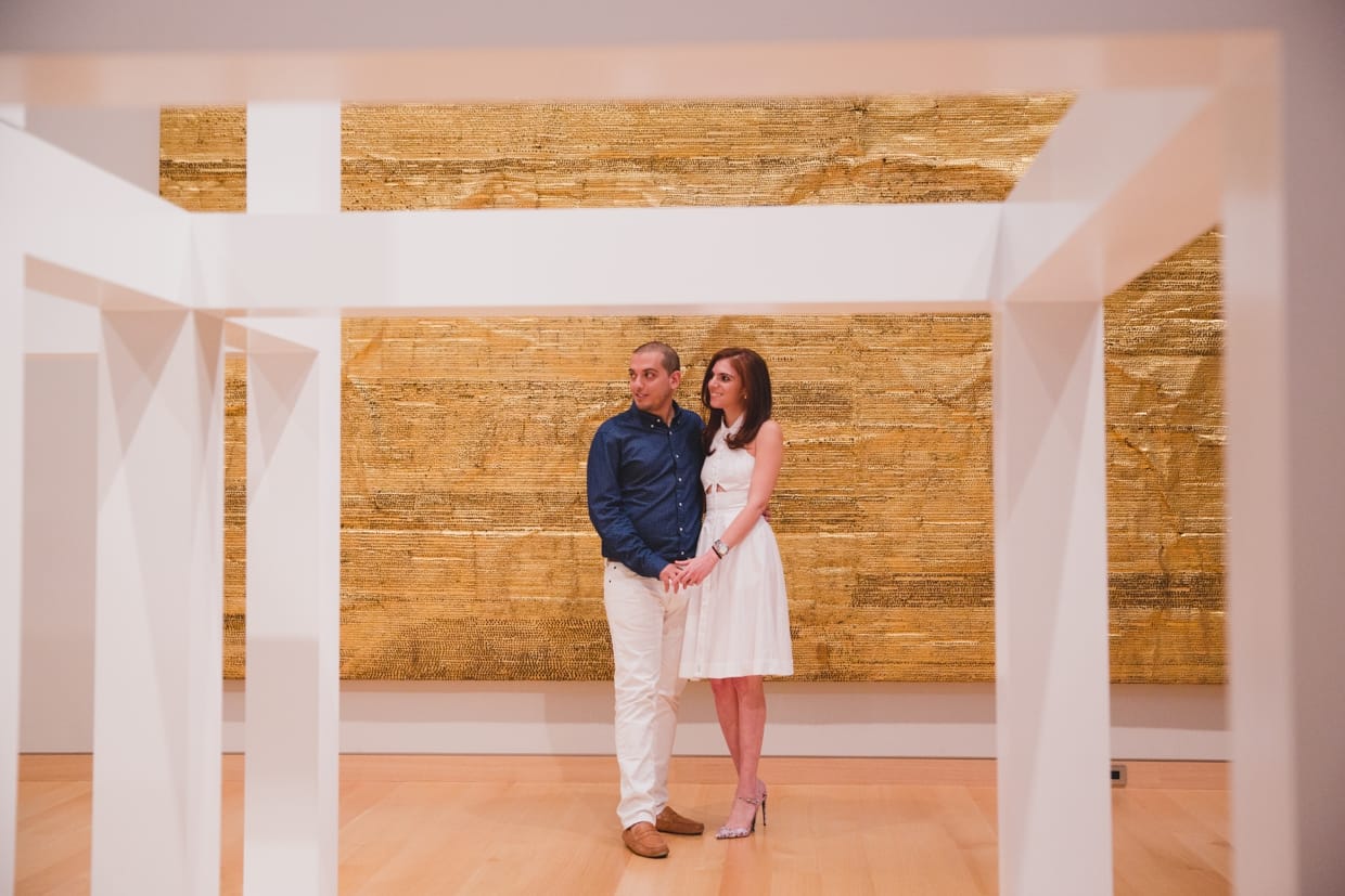 A couple hold hands and look at various contemporary art pieces during their engagement session at the Museum of Fine Arts