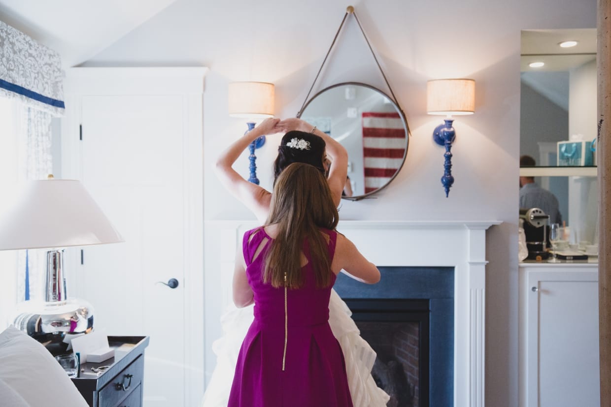 A bridesmaids helps the bride fasten her wedding dress before her backyard wedding in Massachusetts