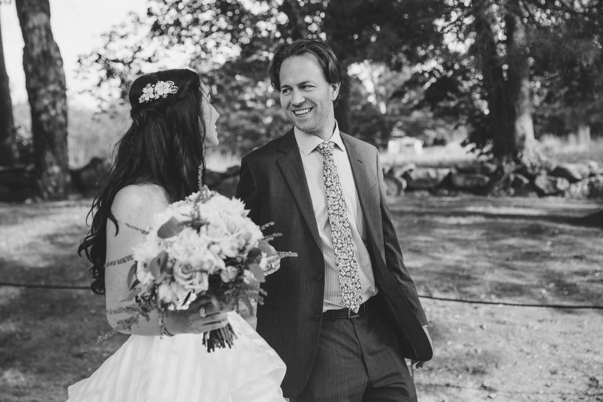 A relaxed and fun photograph of a bride and groom walking through the Minute Man Park before their backyard wedding in Massachusetts