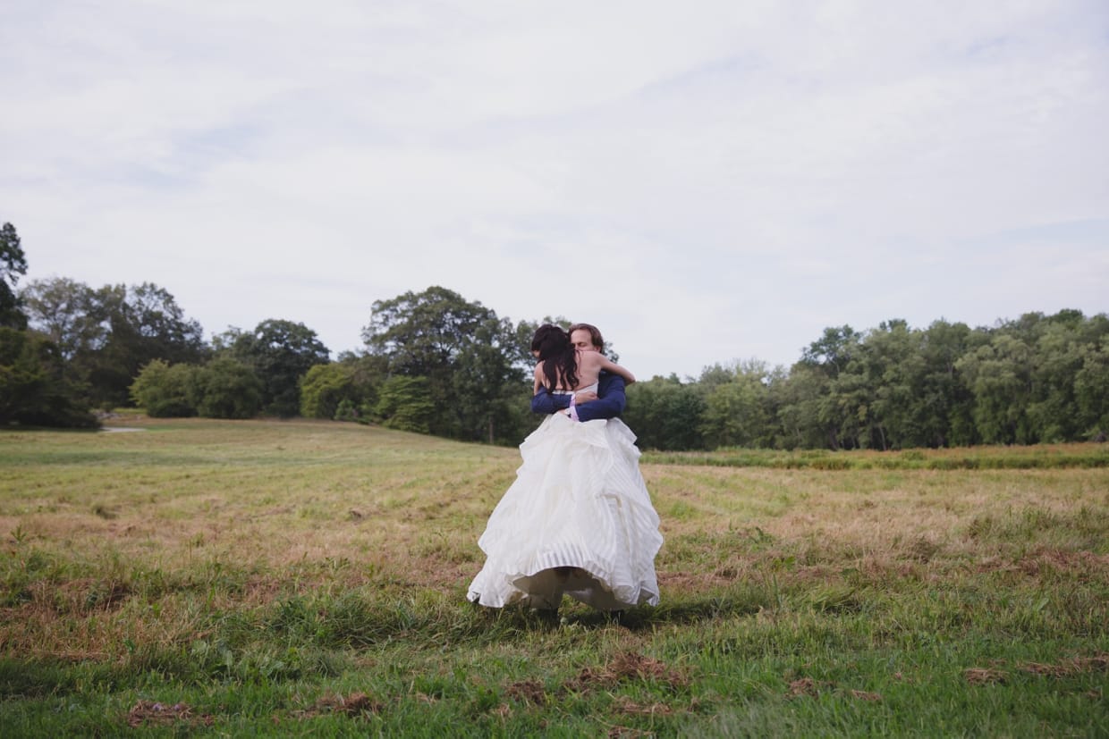 An amazing portrait of a groom spinning his bride around in the Minute Man Park before their backyard wedding in Massachusetts