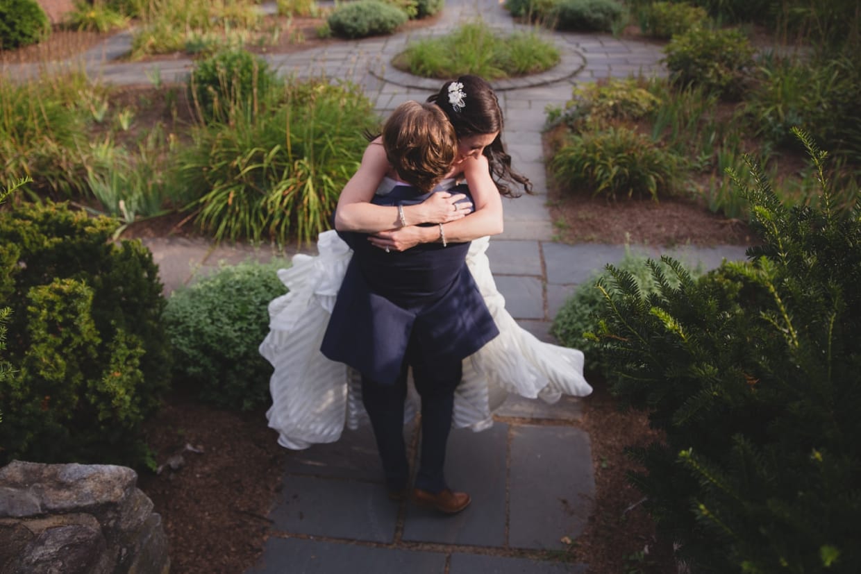 A sweet photograph of a bride and groom spinning around in the garden of the Minute Man Park before their backyard wedding in Massachusetts