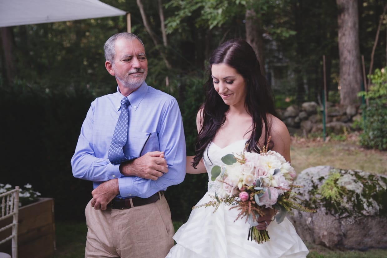 A father walks his daughter down the aisle during a backyard wedding ceremony in Massachusetts