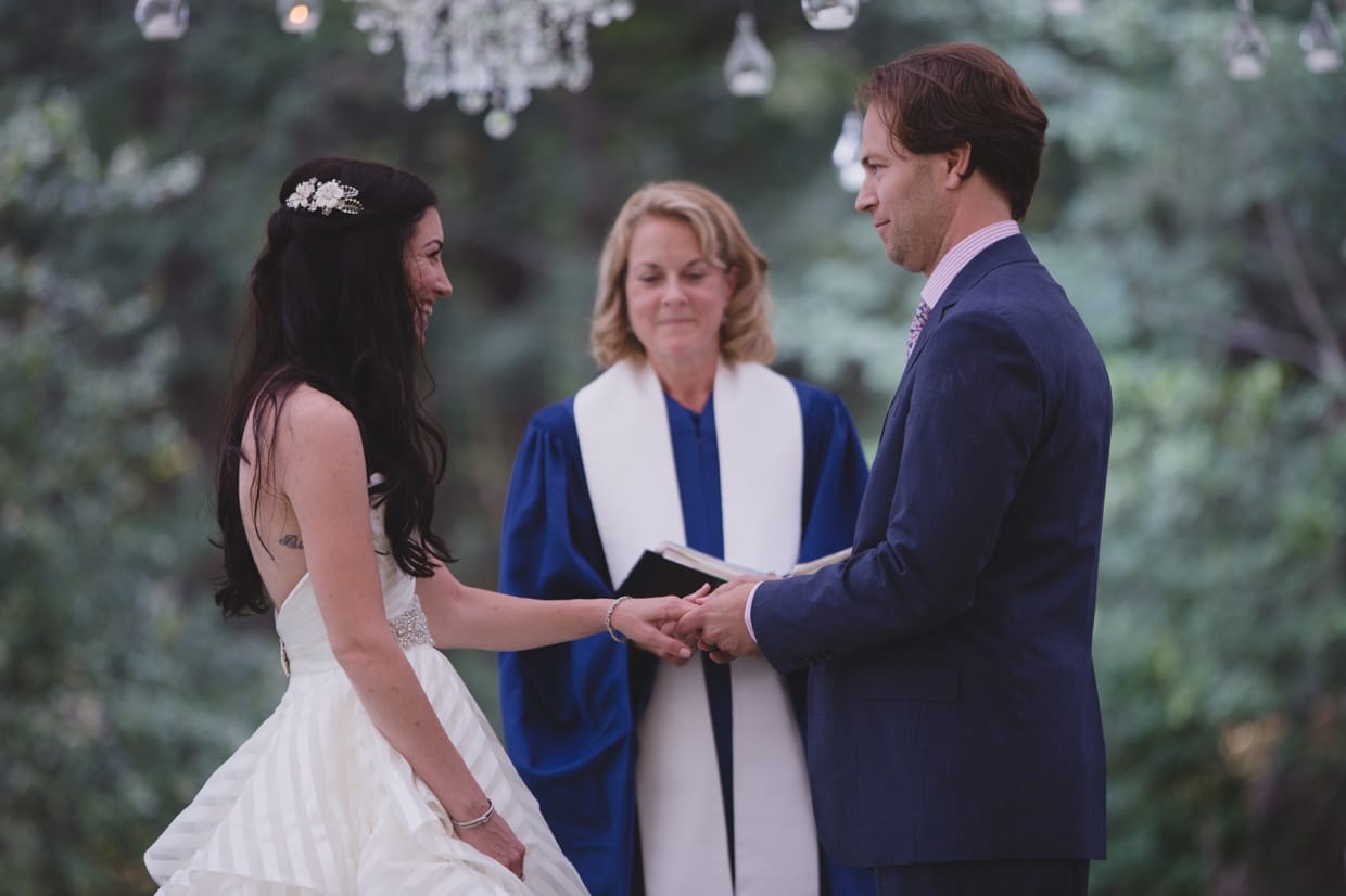 A bride smiles as her husband places a ring on her finger during their backyard wedding ceremony in Massachusetts