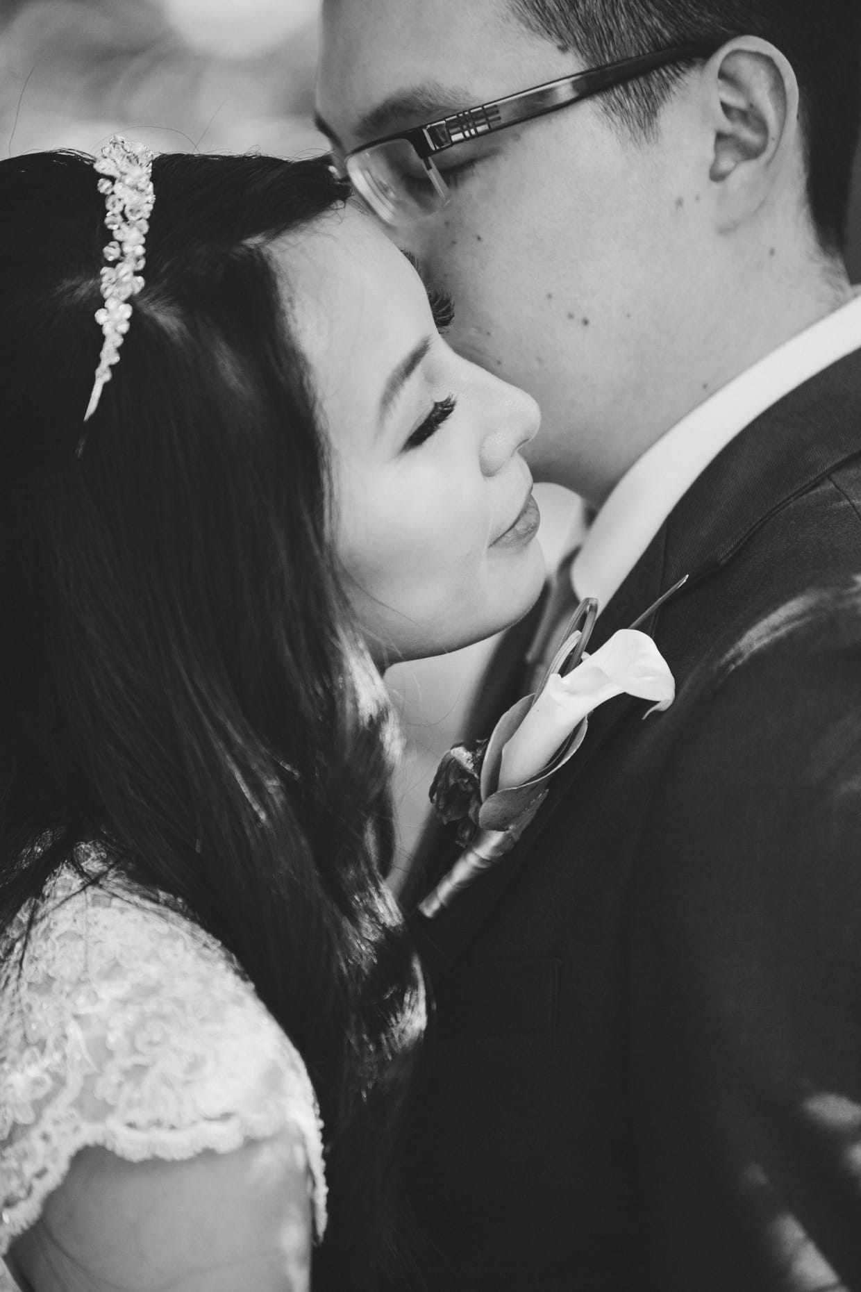 A beautiful photograph a groom kissing his bride on the cheek during their first look at the Arnold Arboretum in Boston, Massachusetts