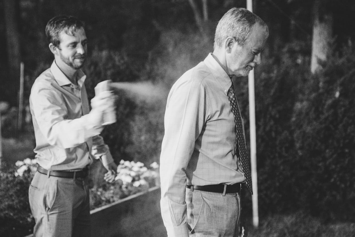 A documentary photograph of wedding guests spraying bug repellant on themselves during a backyard wedding in Massachusetts