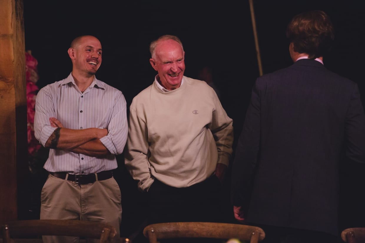 A documentary style photograph of a groom talking to his family during his backyard wedding in Massachusetts