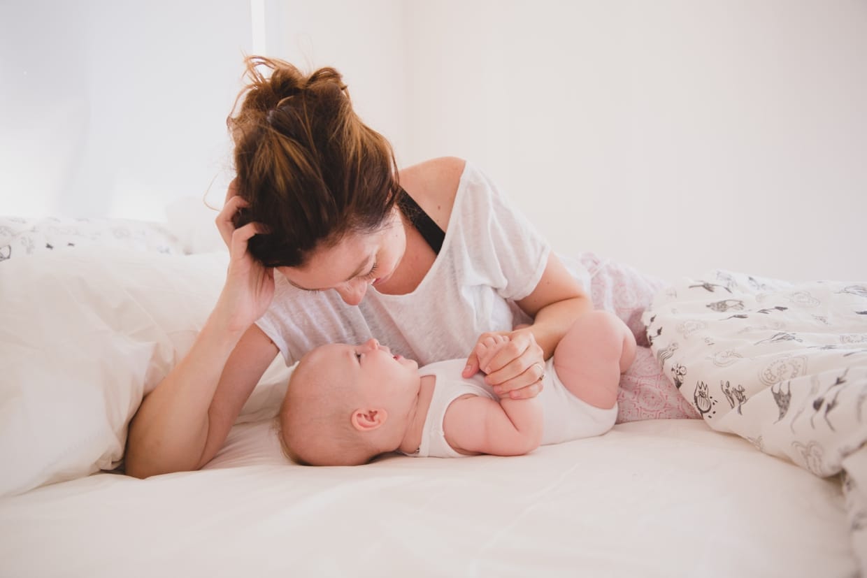 A sweet and intimate photograph of a mother laying with her baby in bed during their in home family photo session in Boston