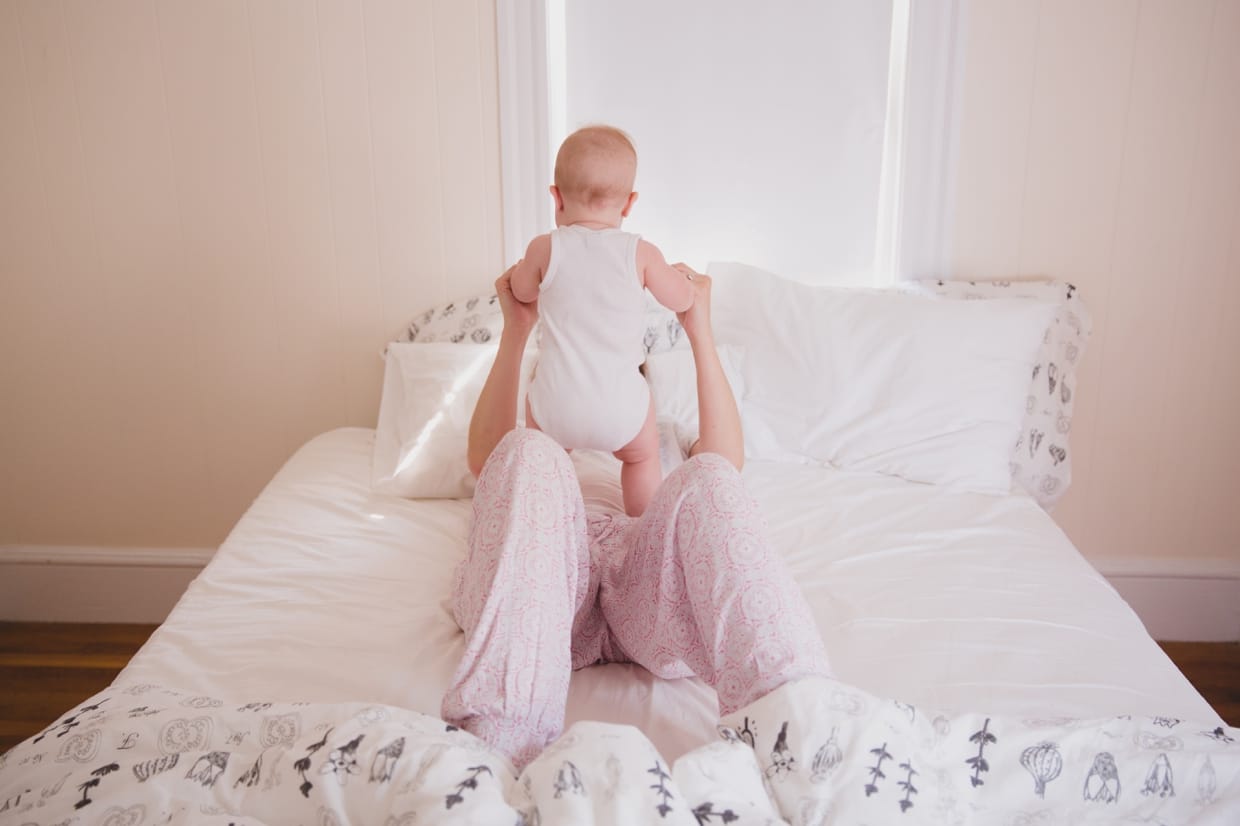 A cute photograph of a mother playing with her baby in bed during a Boston Family Photo Session in Boston