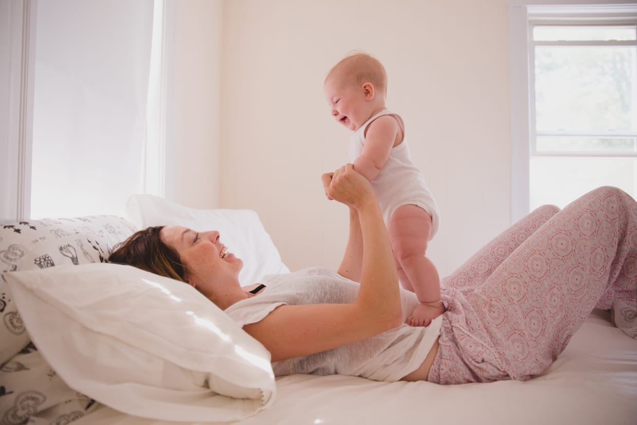A cute photograph of a mother holding her baby in bed during an in home family photo session in Boston