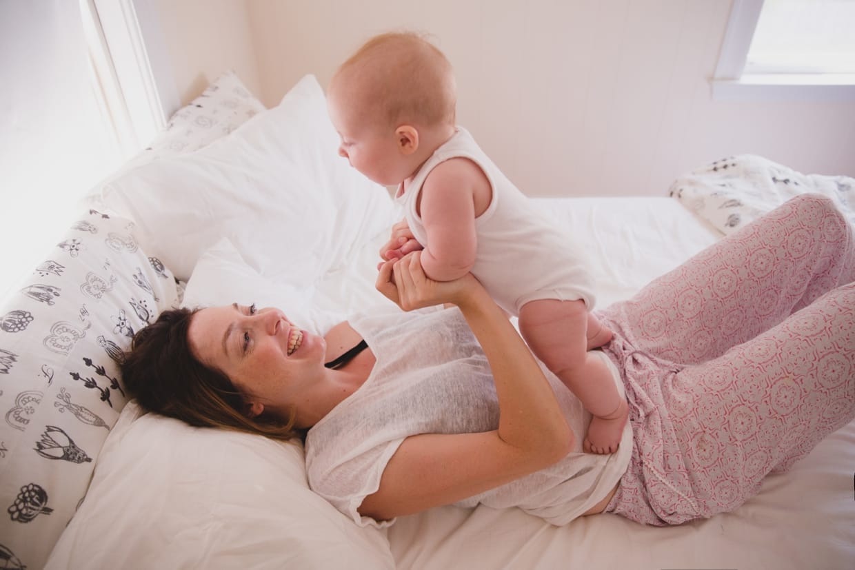 A sweet photograph of a mother playing with her baby in bed during their Boston in home family photo session