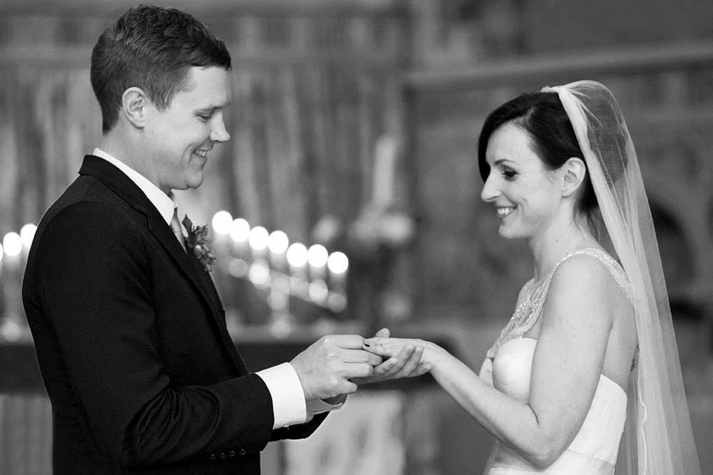 A documentary style photograph of a bride and groom exchanging wedding rings