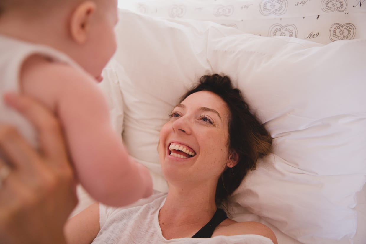 A sweet and intimate photograph of a mother playing with her baby in bed during an in home family photo session in Boston
