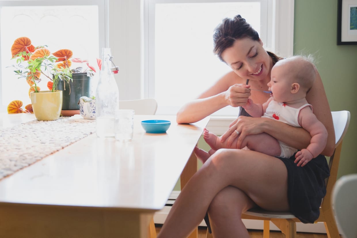 A sweet photograph of a mother feeding her baby at the table during an in home family photo session in Boston