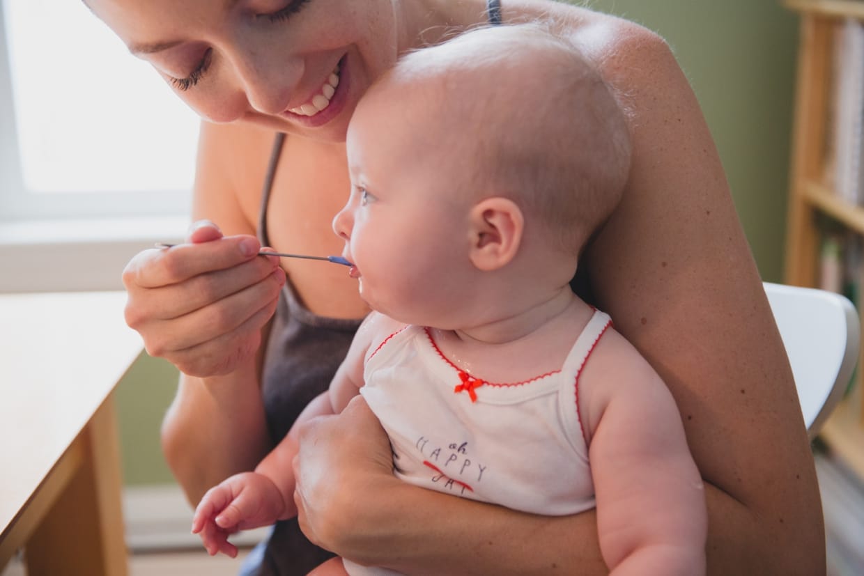 A cute photograph of a mother feeding her baby solids during an in home family photo session in Boston