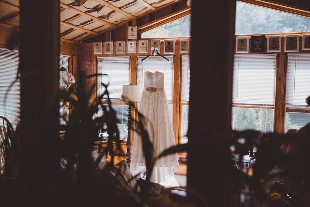 A documentary photograph of a bride's rustic and vintage wedding dress hanging up in her family home on the morning of her rustic River Club Wedding in Scituate, Massachusetts