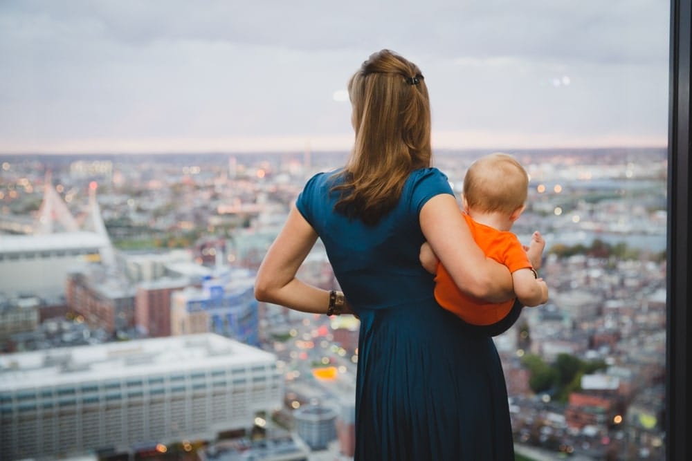 A documentary photograph of a wedding guest and her baby looking out the window during a wedding at the State Room in Boston, Massachusetts