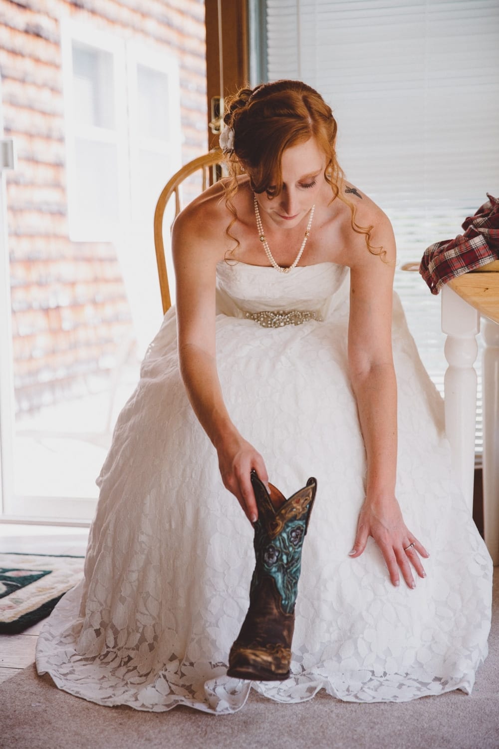 A documentary photograph of a bride putting on her brown and turquoise cowboy boots while getting ready for her rustic River Club Wedding at her family home in Scituate, Massachusetts