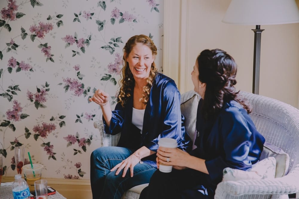 A documentary photograph of two bridesmaids talking and laughing while getting ready at the Governors Inn before a rustic barn wedding at Kitz Farm in New Hampshire