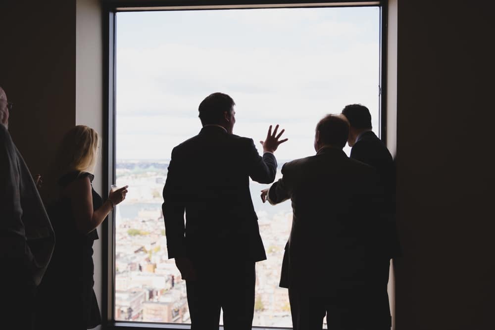 A documentary photograph of wedding guests looking out the window during a wedding at the State Room in Boston, Massachusetts