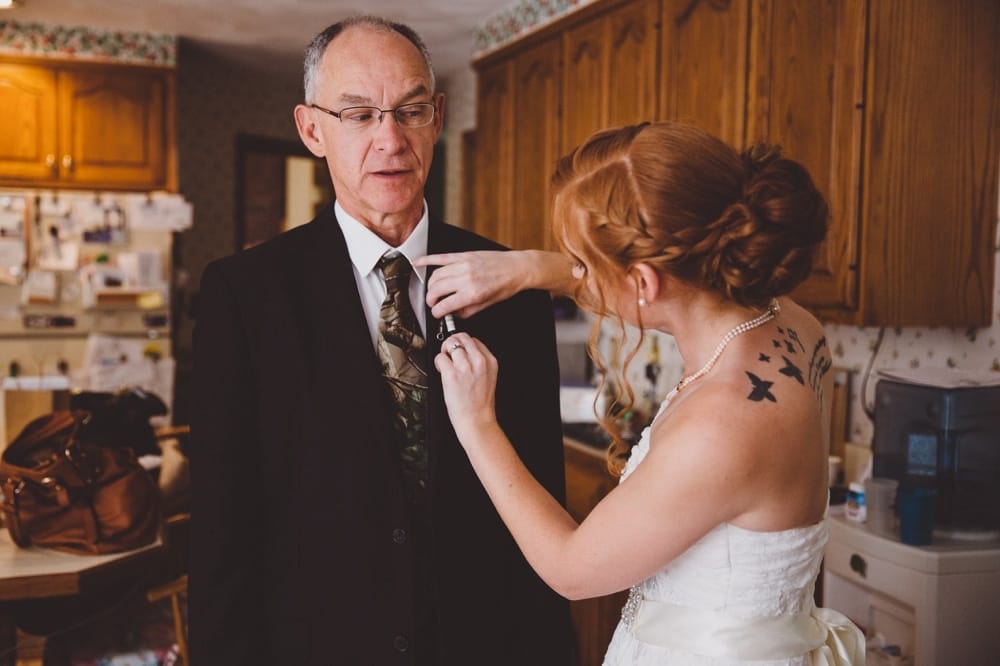 A photojournalistic photograph of a bride putting a handmade boutonnière on her dad before her rustic River Club Wedding in Scituate, Massachusetts