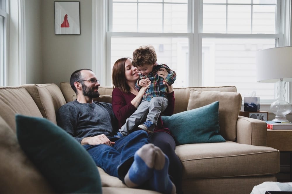 A documentary photograph of a family playing on the couch during their in home family session in Boston, Massachusetts