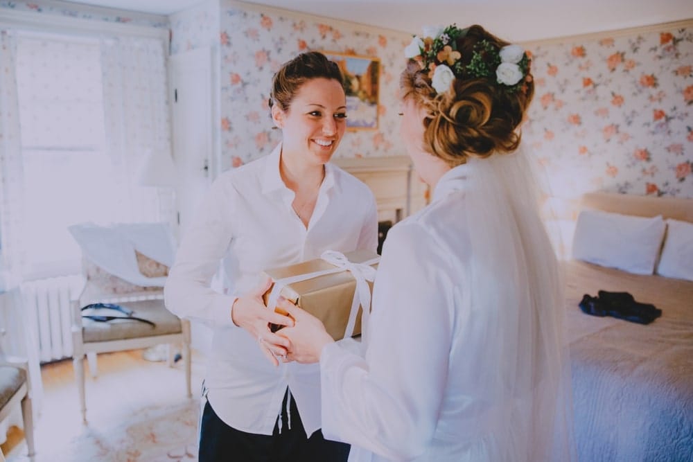 A bride hands her bride a gift before their rustic New Hampshire barn wedding at Kitz Farm